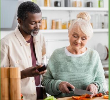 En svart man och en gråhårig kvinna lagar mat tillsammans.
