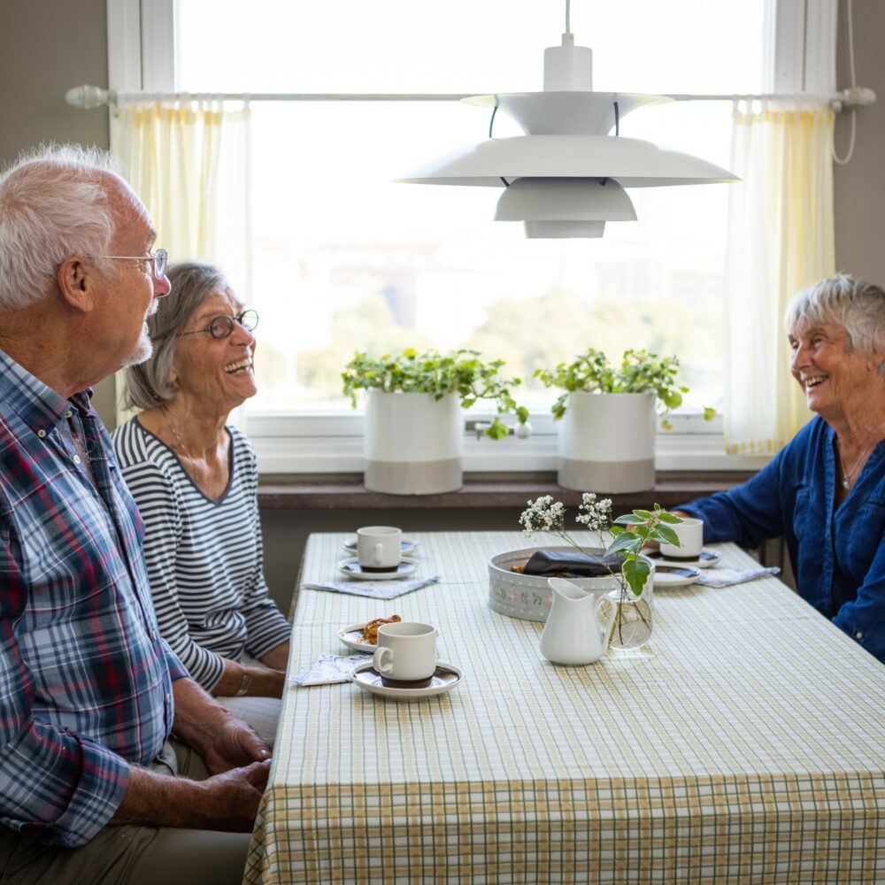 tre äldre personer umgås i gemensam måltid